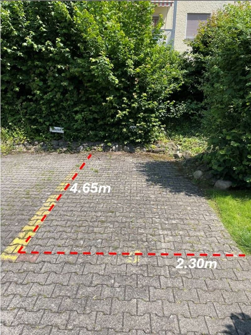 A paved area with a rectangular shape, dimensions marked as 4.65m and 2.30m, surrounded by greenery and a building in the background.