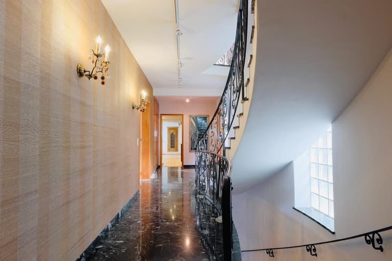 Spacious hallway with marble flooring, ornate wall sconces, and a decorative wrought-iron staircase railing leading to the upper level.