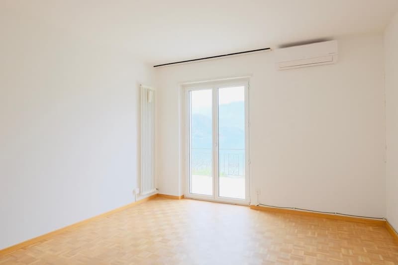 Spacious room with large windows, hardwood floor, and a radiator. The room appears to have access to a balcony or terrace.