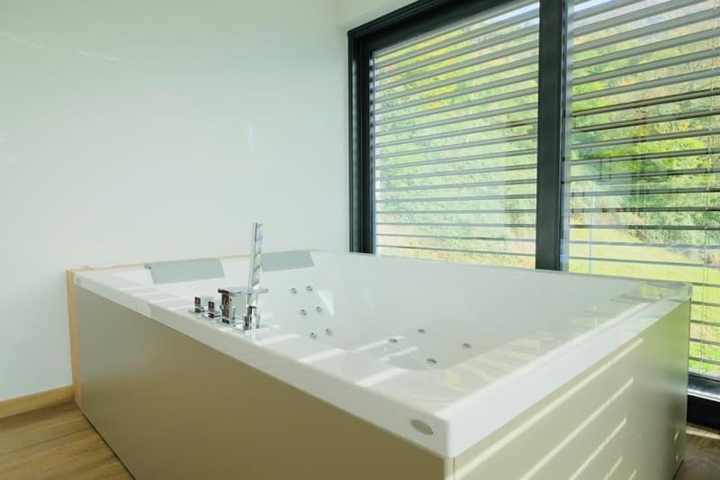 Large white bathtub with jets, surrounded by large windows providing a view of the outdoors