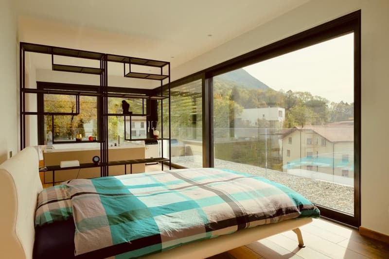 Spacious bedroom with large windows offering a scenic view, modern furniture and decor, plaid bedding