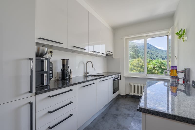 Modern kitchen with white cabinets, black countertops, stainless steel appliances, and large window with a scenic mountain view