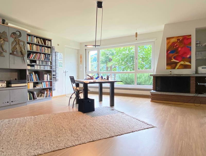 large living room with wooden floor, large windows, fireplace, desk, chair, bookshelf, rug, painting