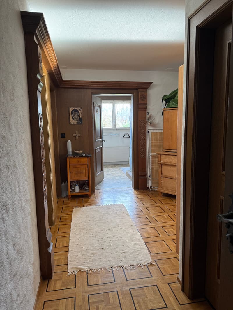 Long corridor with wooden floors, rug, wooden door, hallway leading to a door and window, wooden shelf with items