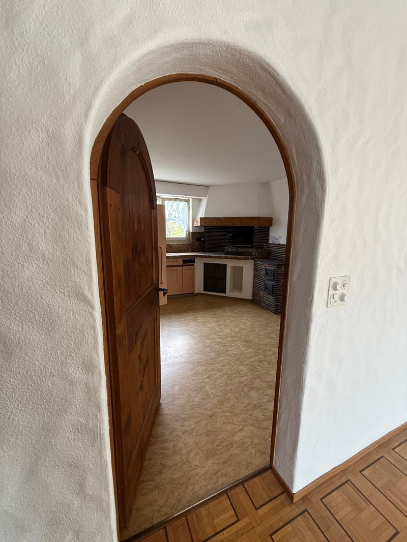 Arch doorway, wooden door, white walls, wooden floor, fireplace, kitchen area, window