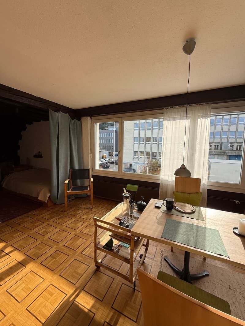 living room with wooden floor, bed, table, chair, lamp, curtains, windows