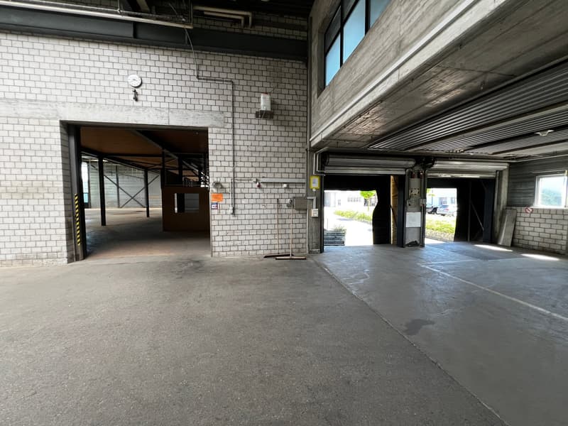 Empty parking lot with white brick walls, two open garages, and a clock on the wall.
