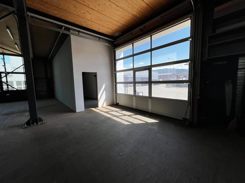 Empty room with concrete floor, white walls, wooden ceiling, large windows, and a door.