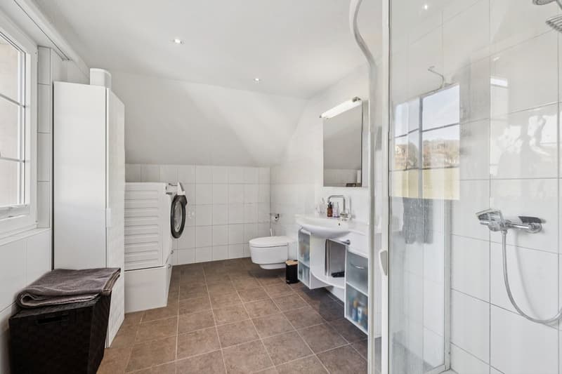 Helles Badezimmer der OG-Wohnung mit Dusche, eigener Waschmaschine sowie eigenem Tumbler