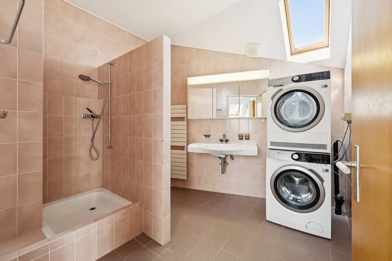 Das Badezimmer im Dachgeschoss überzeugt mit einem WC, Dusche und integriertem Waschturm. Eine komfortable und funktionale Lösung für Wohnalltag.