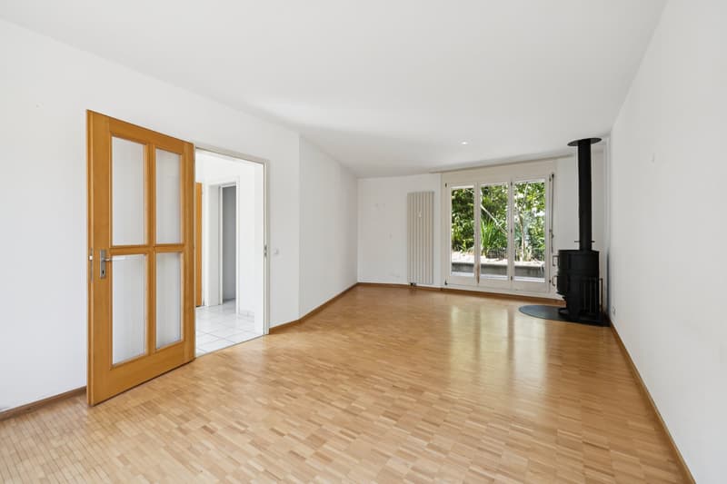 Der helle Wohnbereich mit Schwedenofen schafft eine einladende Atmosphäre und lädt zum Verweilen ein. Der direkte Zugang zum Aussenbereich erweitert den Wohnraum ins Grüne.