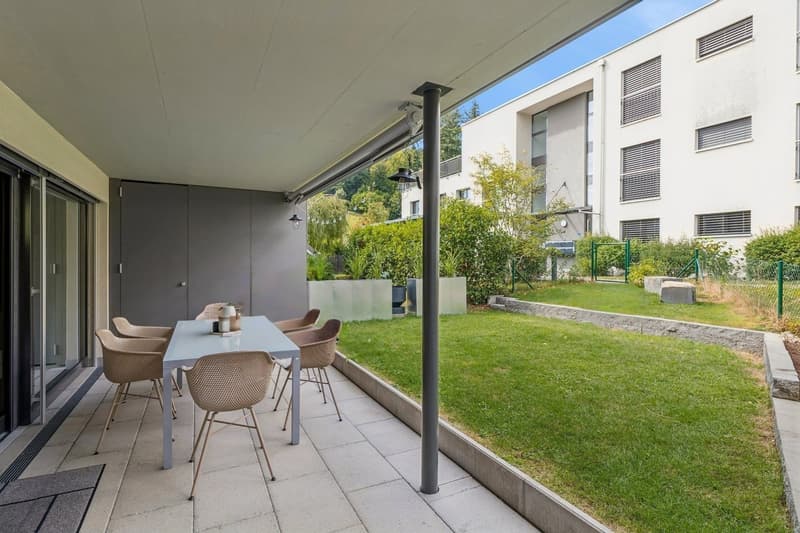 Der barrierefrei zugängliche, überdachte Aussenbereich lädt mit Platz für Esstisch und Grill zum Verweilen ein. Ein praktischer Abstellraum bietet zusätzlichen Stauraum.