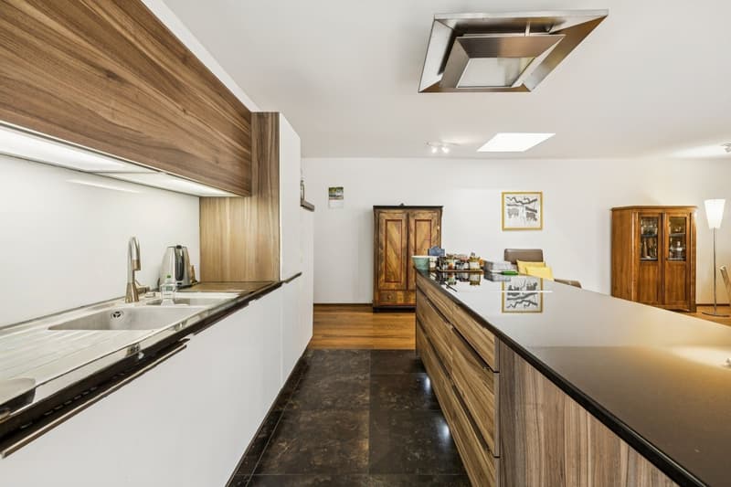 Die moderne Küche fügt sich harmonisch ein. Die Kochinsel bildet den zentralen Treffpunkt für Kochen und geselliges Beisammensein.