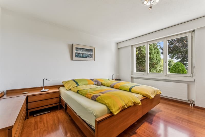 Das grosszügige Schlafzimmer begeistert mit viel Tageslicht und einem edlen Parkettboden, der eine warme und behagliche Atmosphäre schafft