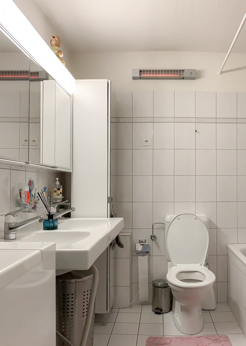 white tiled walls, white sink, white toilet, white bathtub, white mirror, white cabinets, white toilet paper holder, white trash can, white towel rack, white towel, white floor