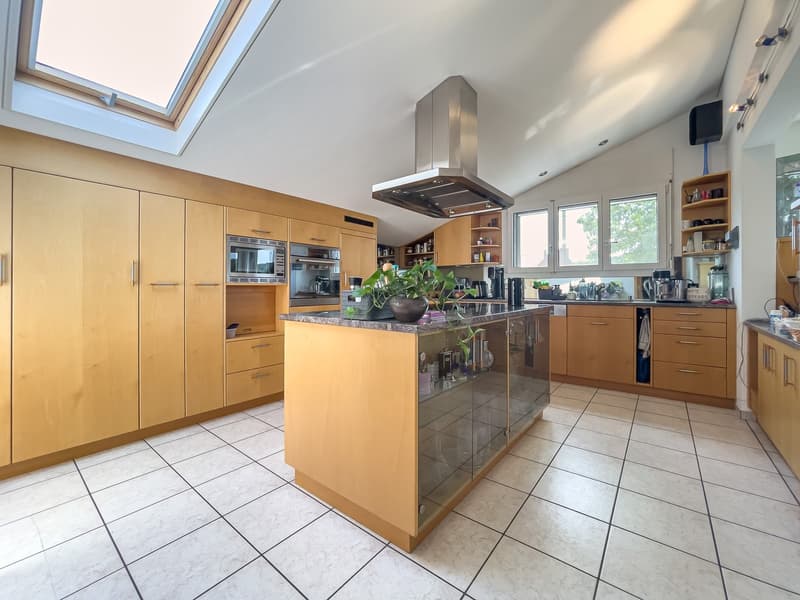 Spacious kitchen with wooden cabinets, stainless steel range hood, tile flooring, and a central island with a granite countertop.