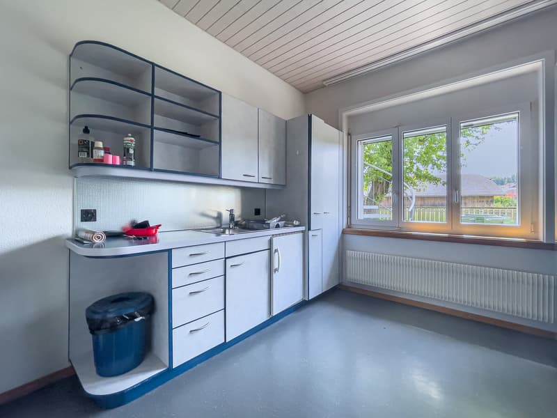 The image shows a modern kitchen with gray cabinets, a sink, and a window overlooking the outdoors. There is a dishwasher visible among the kitchen appliances.