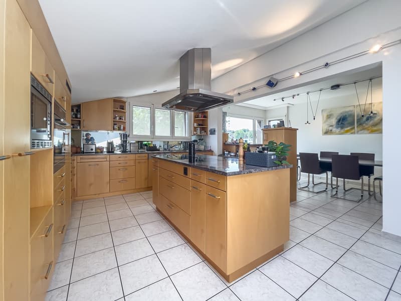 Spacious kitchen with wooden cabinets, granite countertops, stainless steel range hood, tiled flooring, and a dining area with a table and chairs