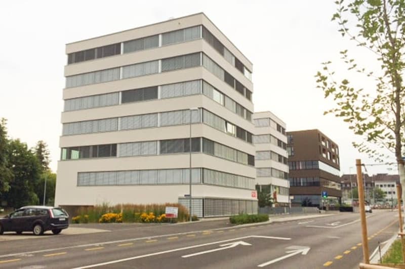 White building, 5 floors, glass windows, street side, small vegetation area, car parked
