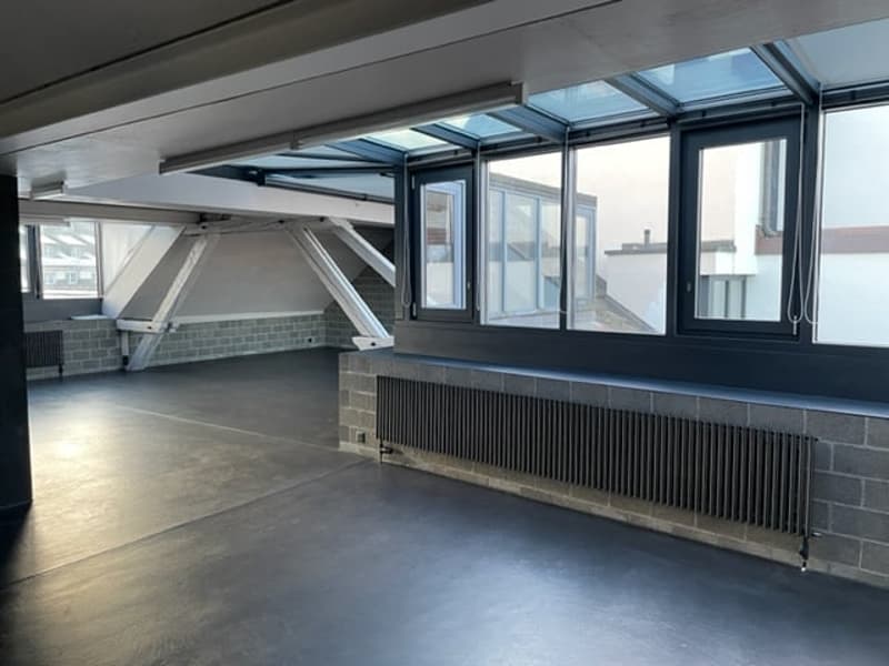 wide room, black floor, large windows, skylight, radiator, brick walls