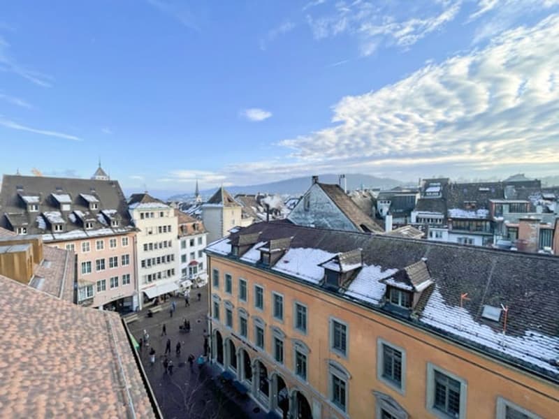 Urban landscape with several multi-story buildings, snow-covered rooftops, and a street with pedestrians