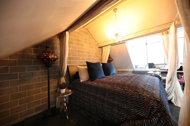 bed with zebra-striped duvet, blue pillows, chandelier hanging from ceiling, brick wall, wooden floor