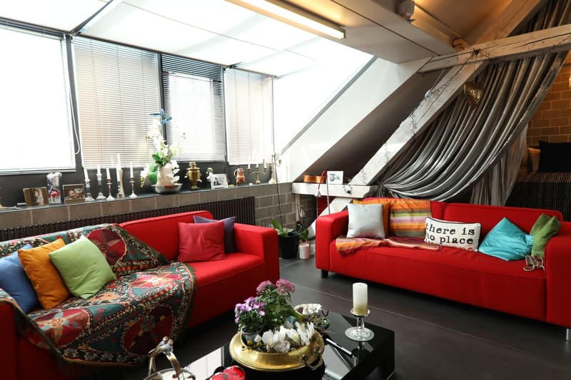 red couches, lots of pillows, window blinds, potted plants, wooden beams, dark hardwood floor