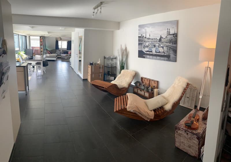 Open floor plan, modern decor, wooden lounge chairs, black tiled floor, white walls, artwork, floor lamp, wooden storage box with violin