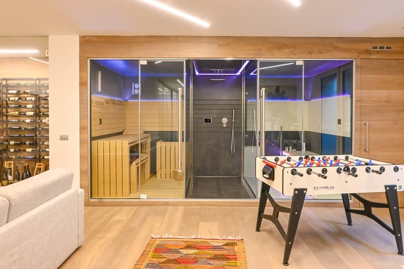 open room with large couch, carpet, glass doors leading to sauna and shower area, foosball table