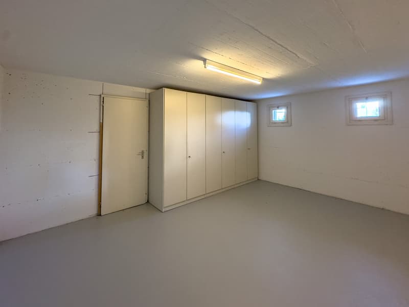Empty room with white walls, ceiling, and floor, a white door, a white cabinet with multiple doors, and two small windows.