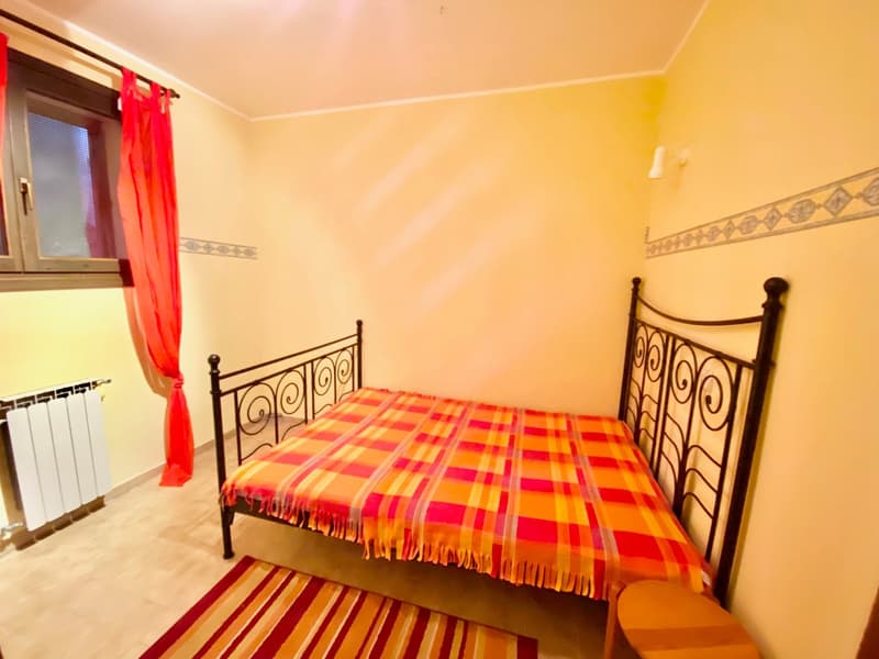 Single bed, radiator, rug, window with red curtains