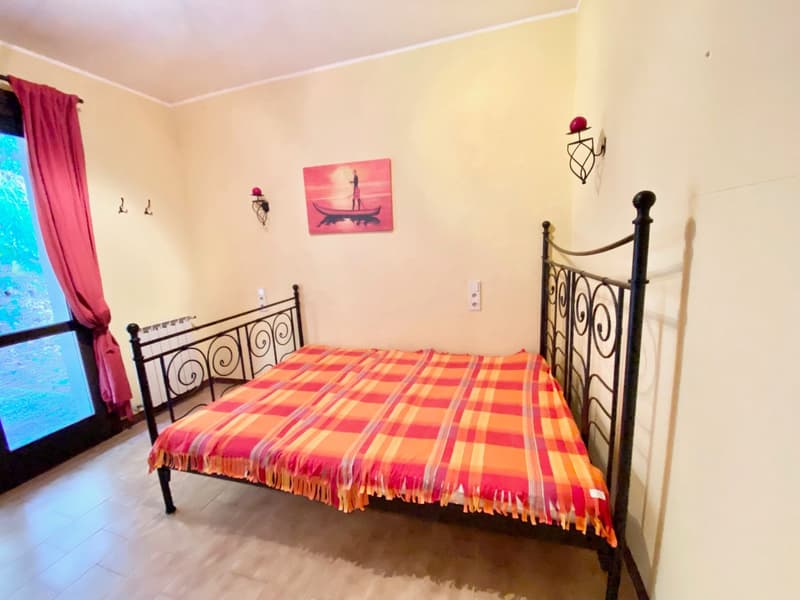 single bed with plaid cover, white tile floor, glass door, wall mounted candle holders, picture frame
