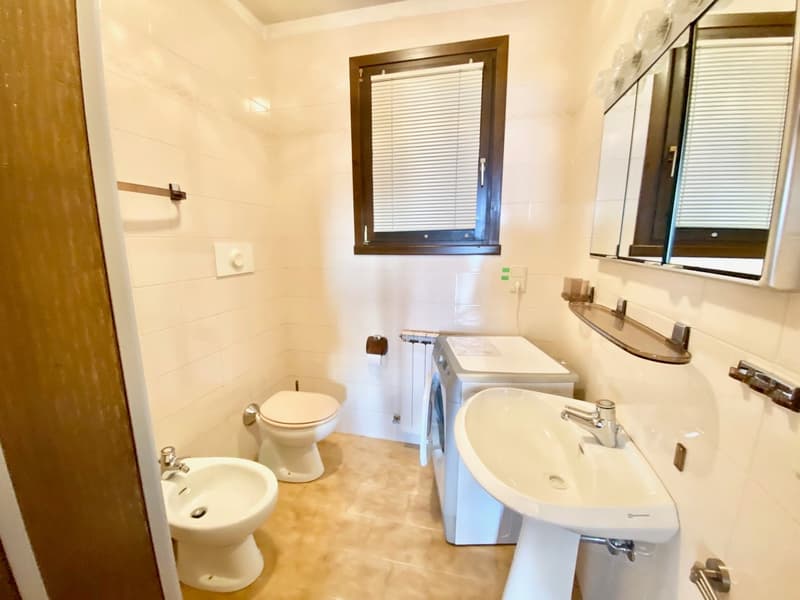 white tiles, white sink, white toilet, bidet, washing machine, mirror, window with blinds