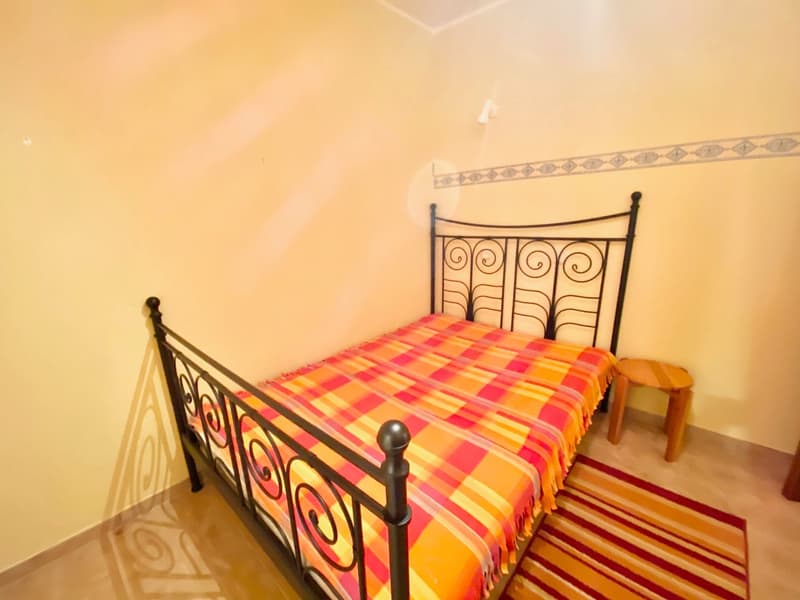 A bedroom with a bed, a stool, and a rug on the floor.