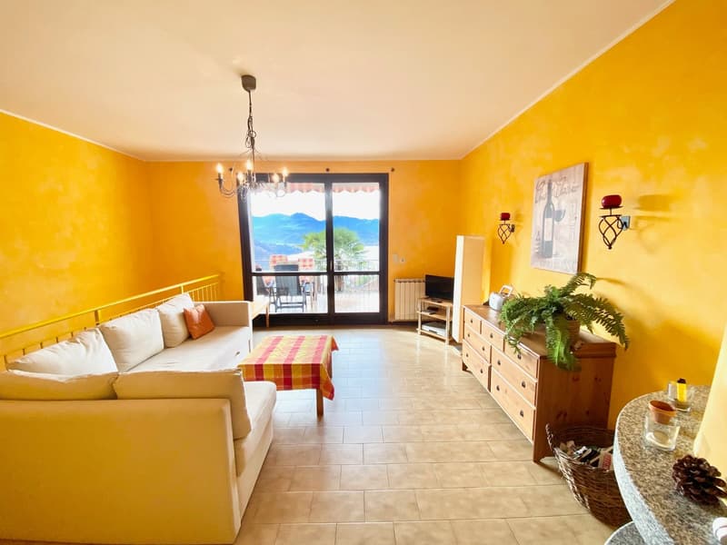 Bright living room with yellow walls, white couch, coffee table, chandelier, wooden cabinet, potted plant, balcony with view