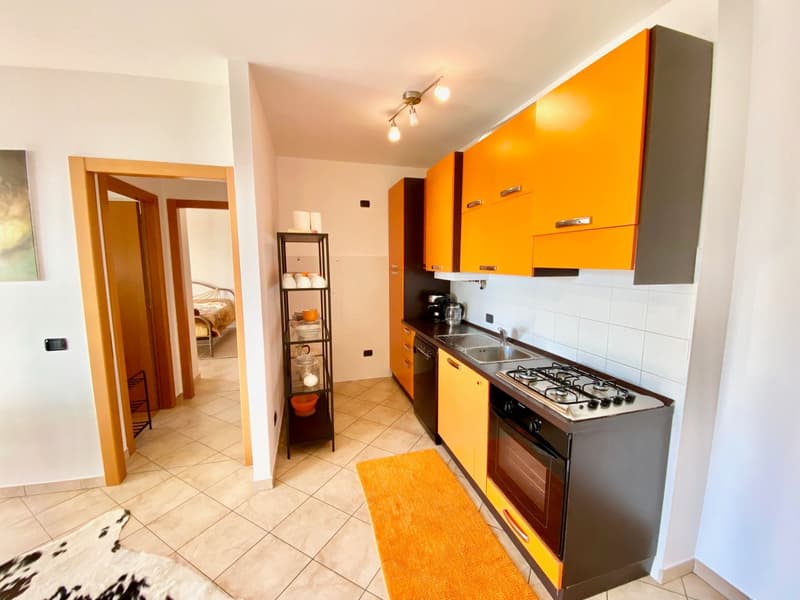 modern kitchen, orange cabinets, tiled floor, gas stove, sink, faucet, overhead lighting, shelves, rug