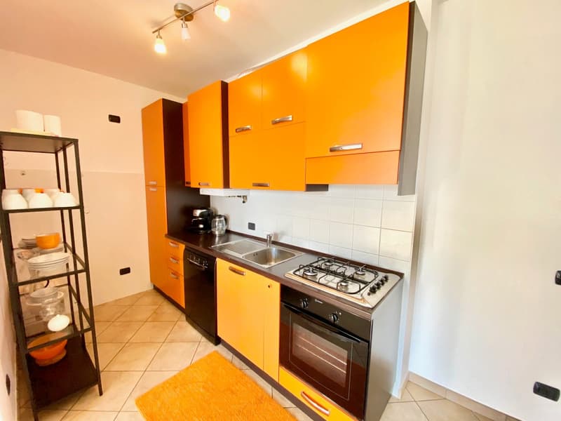 Compact kitchen with yellow cabinets, modern sink, four burner gas stove, built-in oven, white tiles, and floor-mounted black appliances.