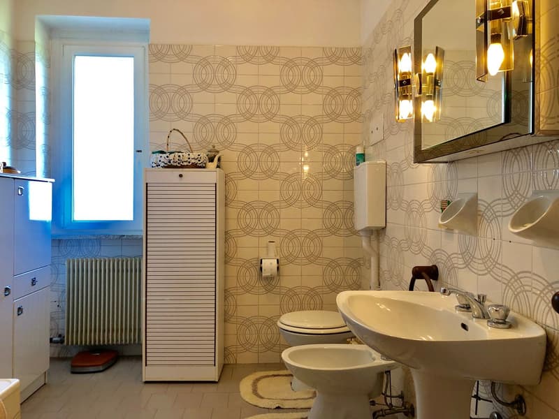 Bathroom with patterned tile walls, a sink with a mirror above, a toilet, and a washing machine cabinet.