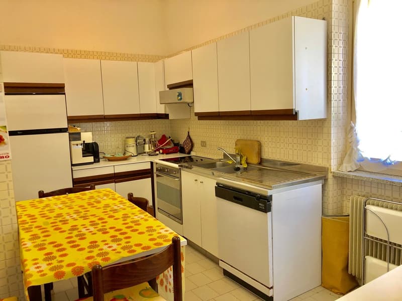 Retro-style kitchen with white cabinets, tiled backsplash, stove, oven, refrigerator, and a yellow patterned table with chairs