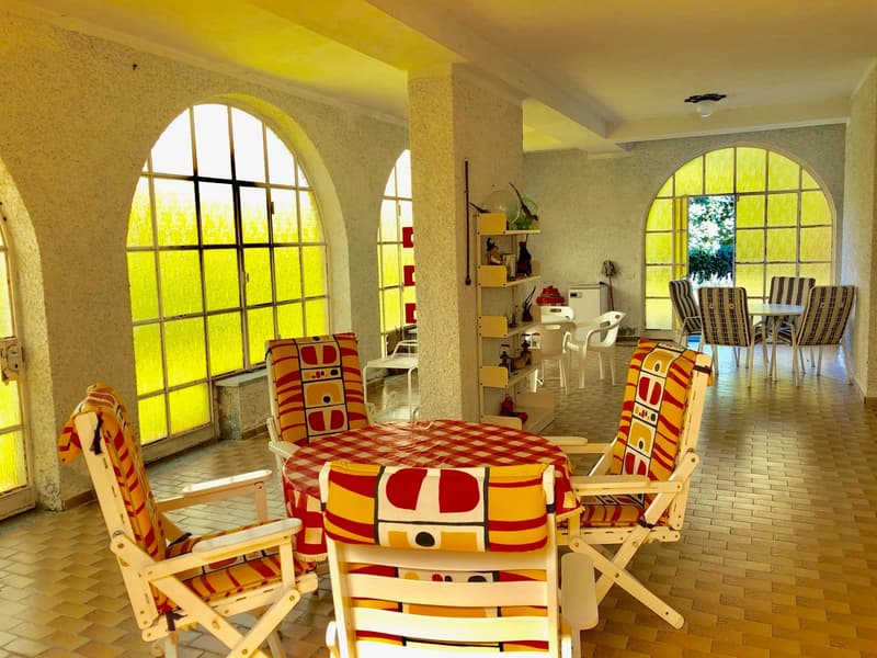 Spacious dining area with arched windows, colorful patterned chairs and table, shelving unit, and tiled flooring