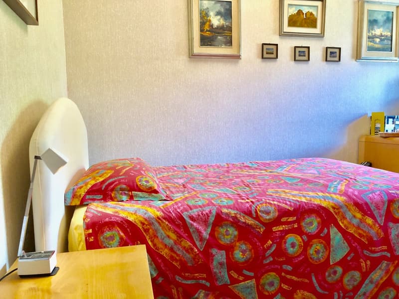 Bedroom with colorful patterned bedding, framed artwork on the walls, and a lamp on the nightstand.