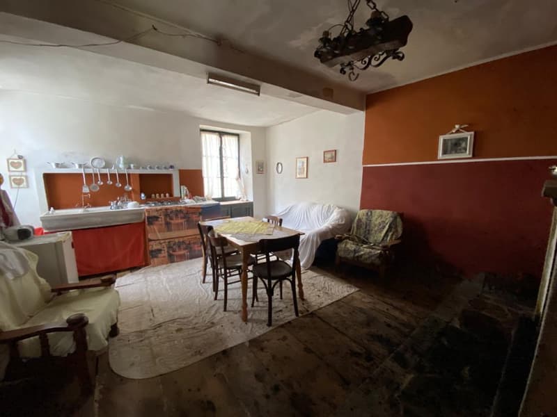 Room with wooden floor, dining table with chairs, two armchairs, chandelier, white walls with red stripes, shelves with kitchenware, and framed photos on the wall