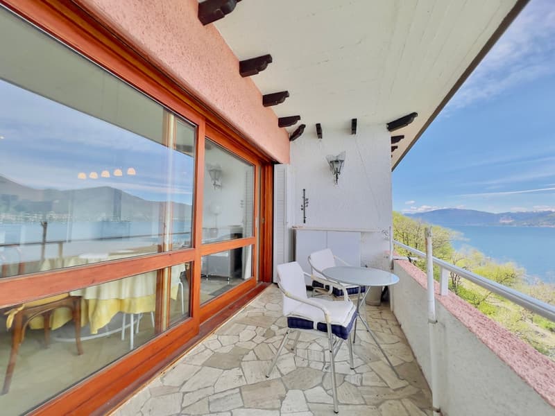 Spacious balcony with large windows, wooden beams, and outdoor furniture overlooking a scenic lake and mountain view