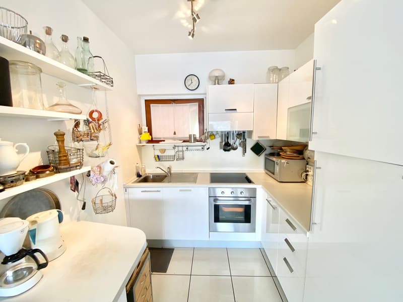 Bright and modern kitchen with white cabinets, open shelving, stainless steel appliances including a dishwasher, and tiled flooring.