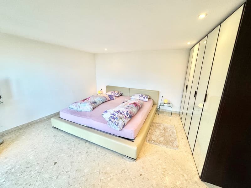 Spacious bedroom with a large bed, floral bedding, and a built-in wardrobe. The room has a tiled floor and recessed lighting.