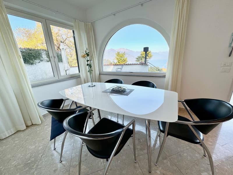 Spacious dining area with large arched window offering a scenic view, white marble-top dining table, black modern chairs, and curtains framing the window