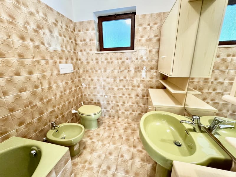 bathroom with bidet, toilet, bathtub, sinks, cabinet, tile walls