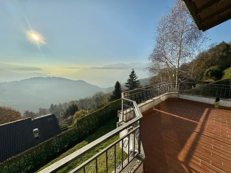 Terrace with panoramic views of mountains and landscape, tiled floor, railing, and a tree in the background.