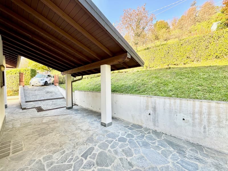 covered parking area with stone pavement, white columns, car parked, sloped grassy area