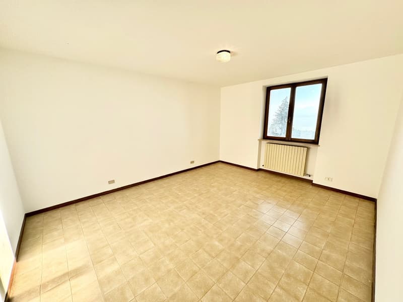 Empty room with white walls, beige tiled floor, a window with a view, and a radiator.